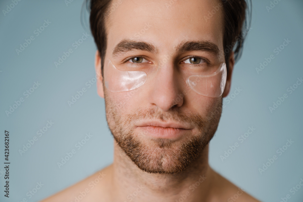 Shirtless white man with under eye patches looking at camera