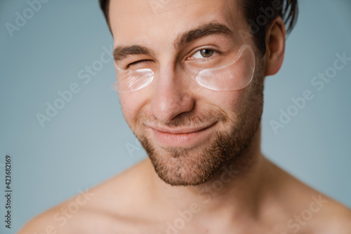 Shirtless white man with under eye patches winking at camera