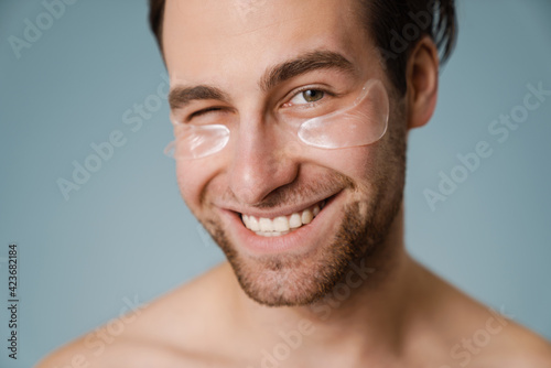 Fototapeta Shirtless white man with under eye patches winking at camera