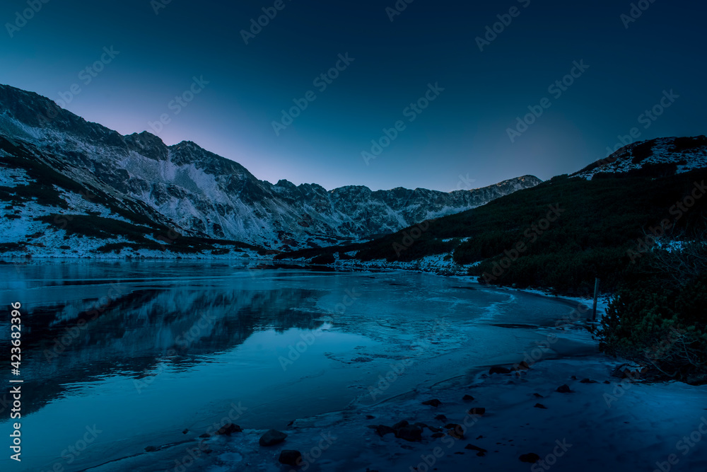 Dark winter night in High Tatra Mountains, The Valley of Five Lakes. Clear sky, windless air and lake starting to freeze. Selective focus on the ridge, blurred background.