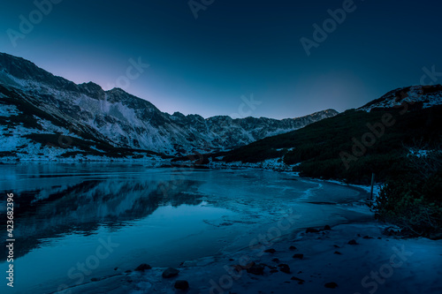 Dark winter night in High Tatra Mountains, The Valley of Five Lakes. Clear sky, windless air and lake starting to freeze. Selective focus on the ridge, blurred background.