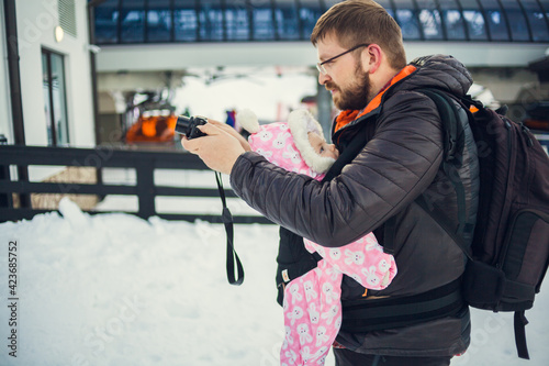 Father with baby child in carrier backpack on snowy street. Family walking at winter. Man photographer blogger vlogger traveling with infant outdoor. Family urban vacations