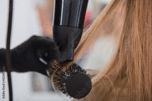Close-up of blow-drying blonde hair with blow-dryer and round brush.