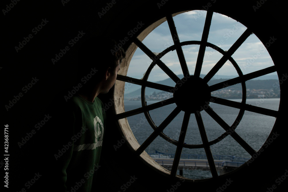 Thoughtful young man looking the river through the window in the shadow