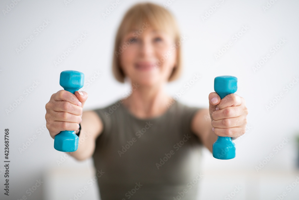 Senior woman doing fitness exercises with weights at home, focus on hands holding dumbbells Senior woman doing fitness exercises with weights at home, focus on hands holding dumbbells