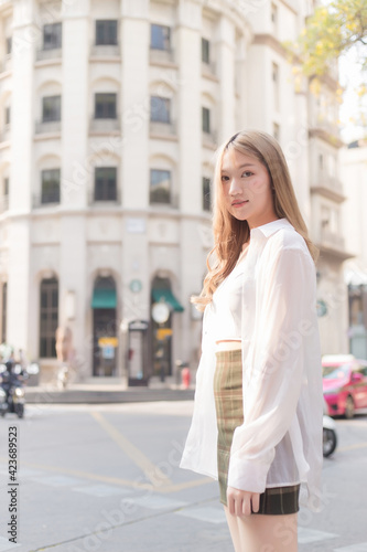 Asian woman with bronze hair in white shirt while walks on street.