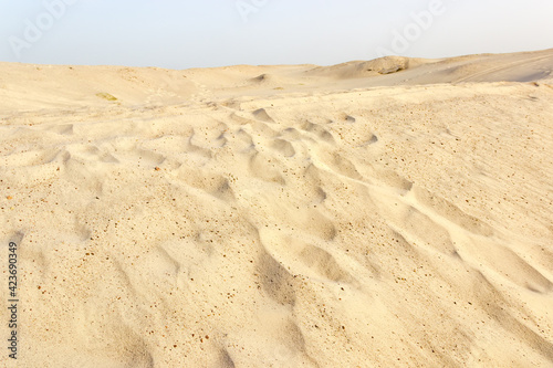 Slope of sandy dune with footprints against clear sky