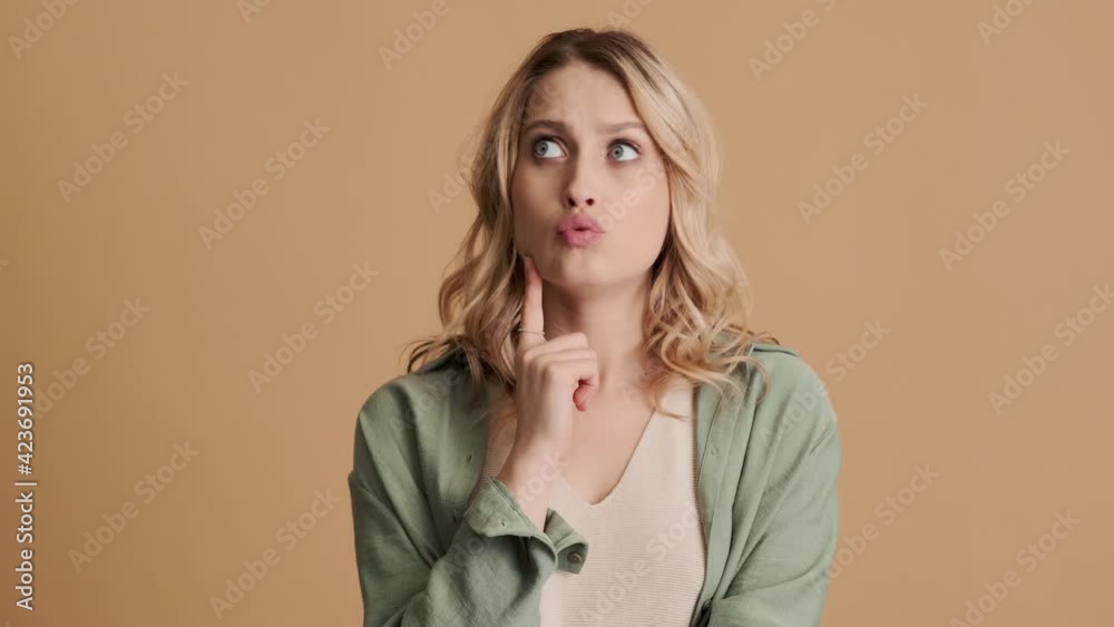 A thinking young woman wearing casual clothes is coming-up with an idea standing isolated over beige background in studio A thinking young woman wearing casual clothes is coming-up with an idea standing isolated over beige background in studio