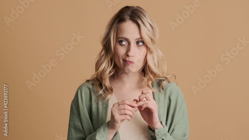 An emotional young woman is nervous standing over beige background in studio photo
