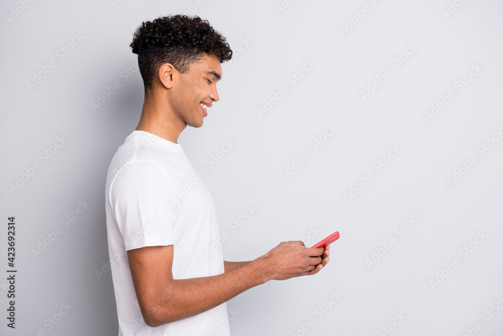 Profile portrait of brunet optimistic nice curly guy hold telephone wear white t-shirt isolated on grey background Profile portrait of brunet optimistic nice curly guy hold telephone wear white t-shirt isolated on grey background