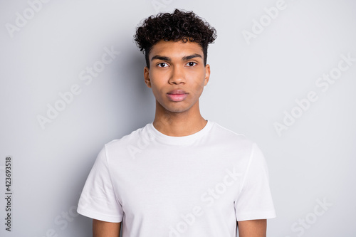 Portrait of brunet serious curly guy wear white t-shirt isolated on grey color background