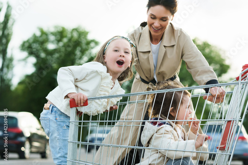 Canvas Print Happy mother and her daughters are having fun with a shopping cart on a parking lot beside a supermarket