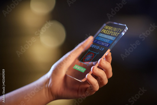technology and health care concept - close up of hand holding transparent smartphone with international certificate of vaccination on screen over white background