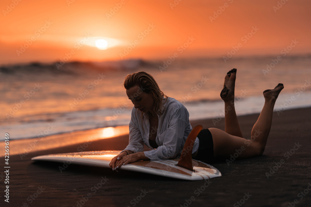 woman on tropical beach holding surfboard at sunset
