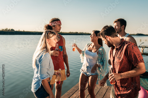 Group of young friends standing of a pier having fun and enjoying a summer day at the lake. © Zoran Zeremski
