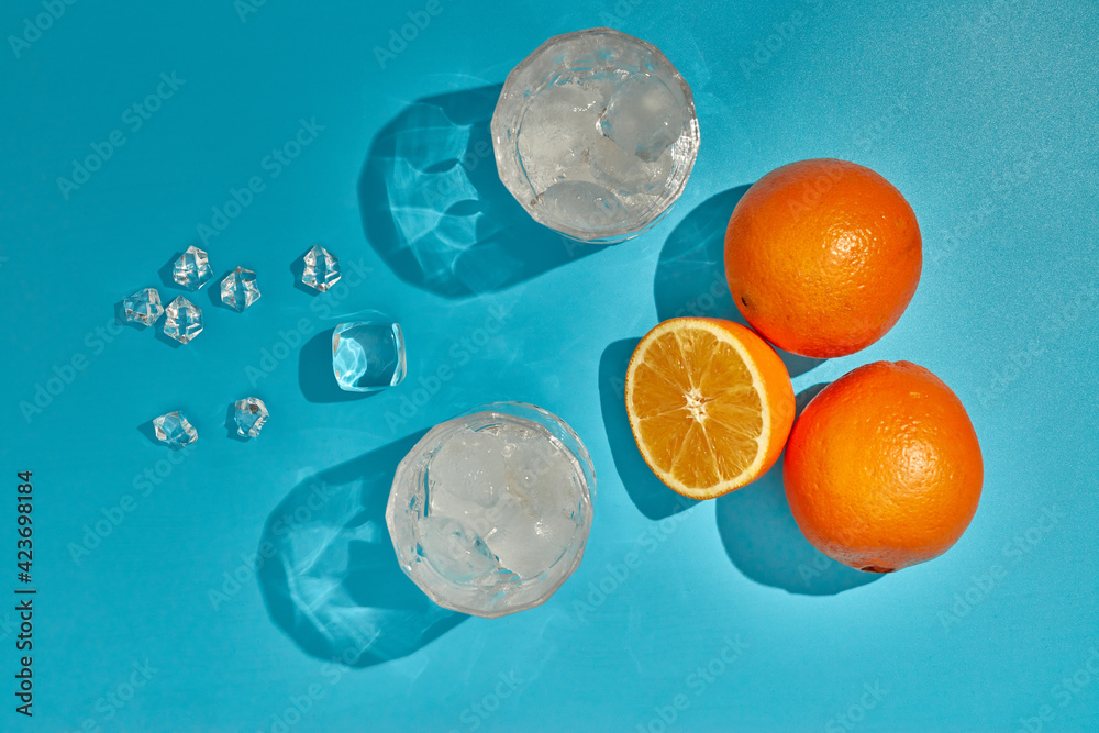 Two glasses with ice and oranges on blue background with shadow. Top view. Cocktail. Fresh orange juice.