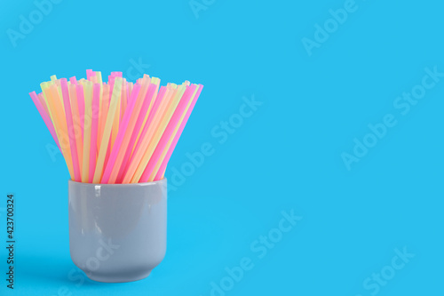 Colorful plastic drinking straws in holder on light blue background, space for text