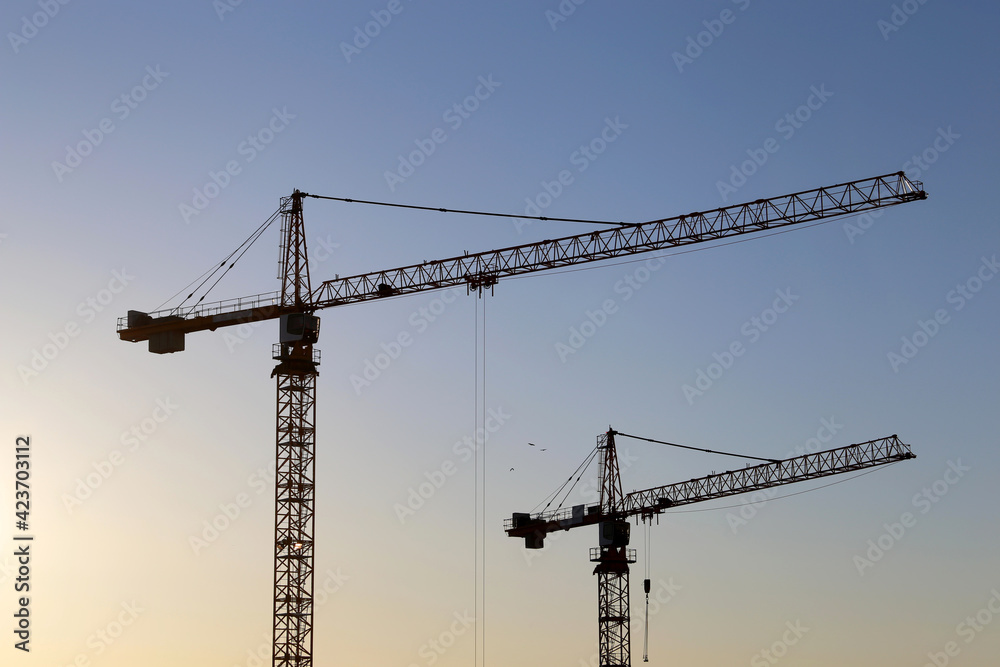 Two tower cranes against blue sky at sunrise. Housing construction