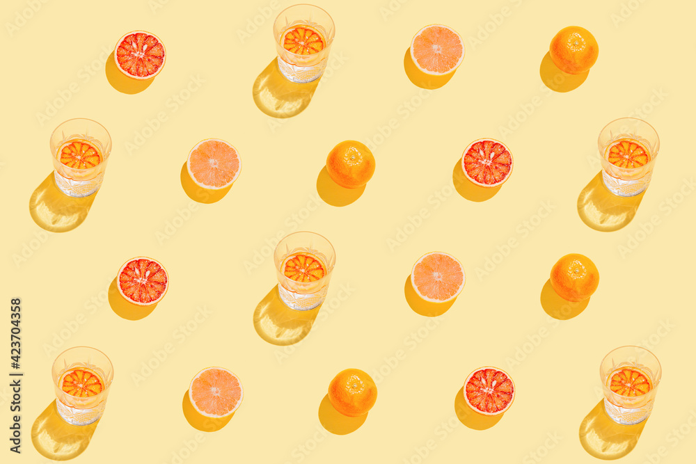 Creative pattern made with sliced grapefruit, blood orange and glass with lemonade or water on yellow background. Summer fruit and refreshment  concept. Minimal style. Sunlit flat lay.