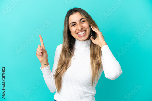 Young caucasian woman using mobile phone isolated on blue background showing and lifting a finger in sign of the best