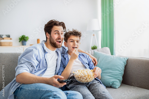 Leisure time at home. Father and son watching movie on TV and eating popcorn  resting on comfortable sofa at home