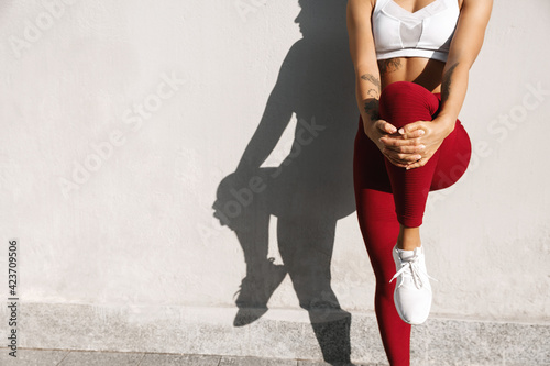 Female athlete warming up before jogging, stretching legs and body for morning run. Sportswoman doing exercises, doing fitness workout, standing against street wall
