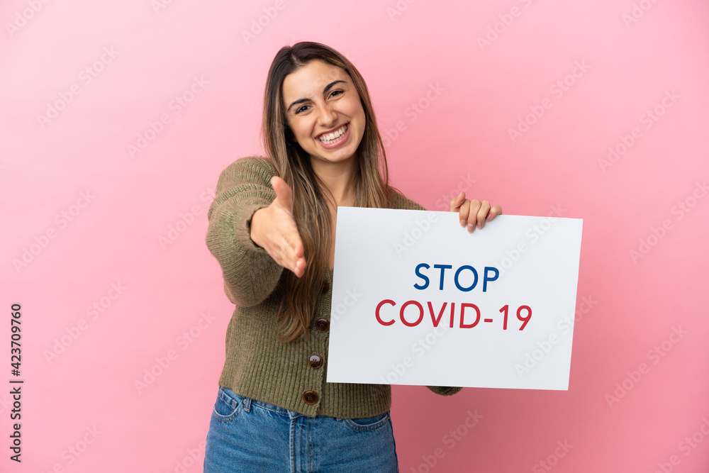 Young caucasian woman isolated on pink background holding a placard with text Stop Covid 19 making a deal