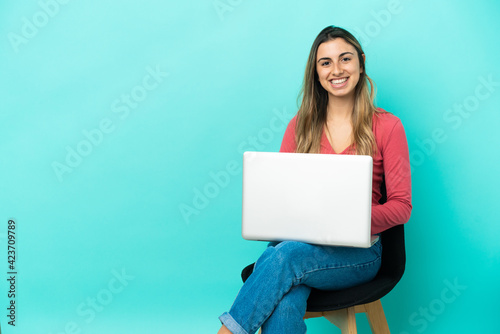 Young caucasian woman sitting on a chair with her pc isolated on blue background laughing © luismolinero