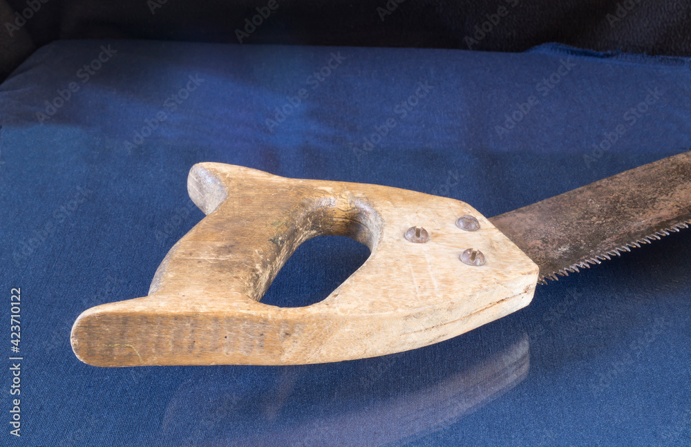 A saw with a wooden handle lies on a table with a reflection A saw with a wooden handle lies on a table with a reflection