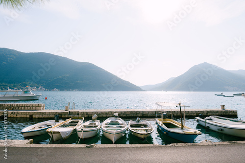 Fishing boats at the pier of the city of Perast against the backdrop of mountains and blue sky.