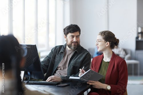 Portrait of bearded business manager talking to female colleague during meeting at table in white office interior