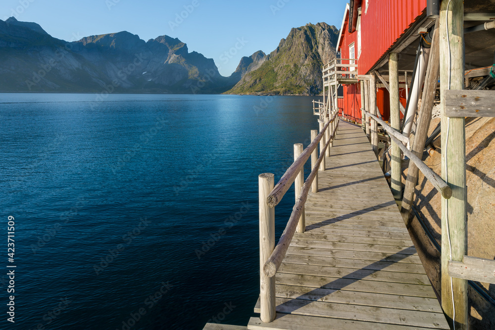 Wooden walk under red wooden fisherman's house in Reine, Lofoten, Norway. Sunset of a sunny day in the village by the sea. Wooden pier and beautiful small wooden house on the shore.