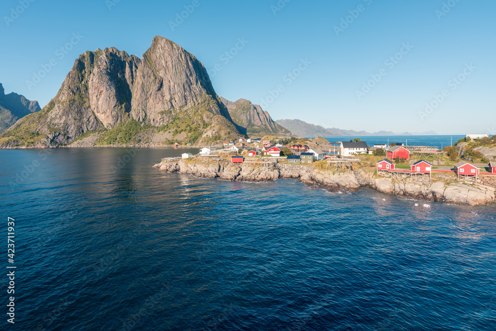 Obraz premium Colorful fisherman's wooden houses in village of Reine in Lofoten in the golden hour. Beautiful sunny afternoon in the arctic. Arctic summer in norwegian fjord. Tall rocks towering above the water.