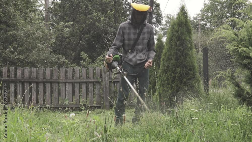 Worker mowing tall grass with electric or petrol lawn trimmer. Gardening care tools and equipment. Process of lawn trimming with hand mower Worker mowing tall grass with electric or petrol lawn trimmer. Gardening care tools and equipment. Process of lawn trimming with hand mower