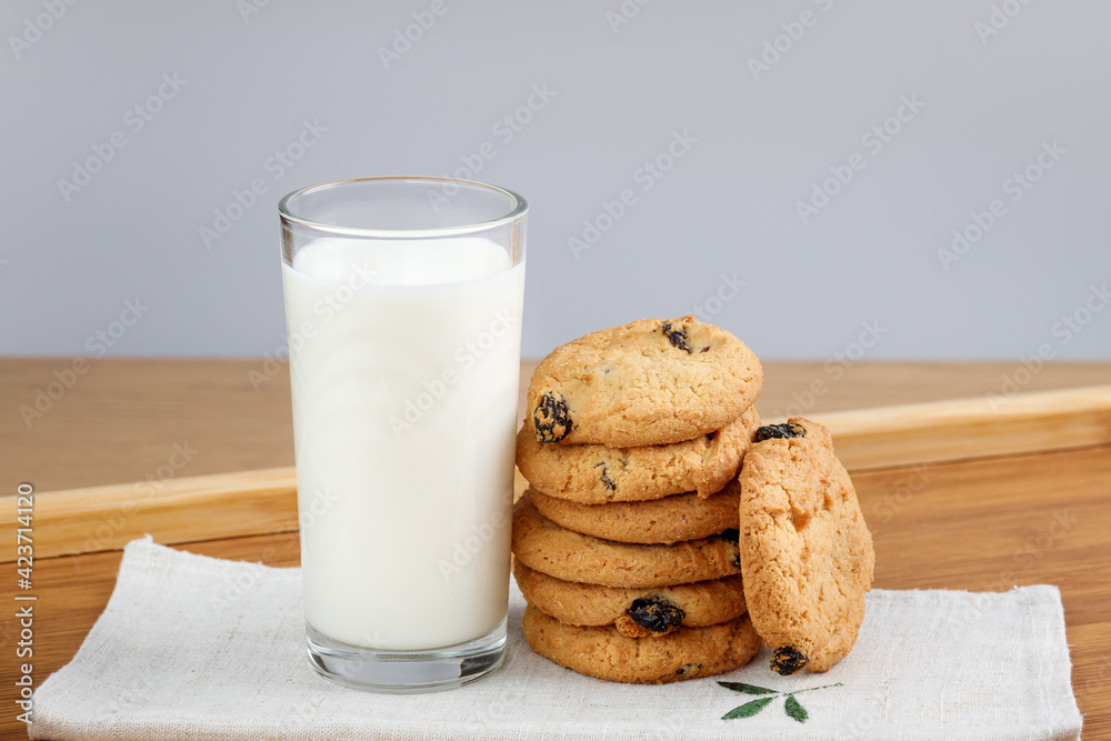 A glass of milk and cookies with raisins on a wooden tray A glass of milk and cookies with raisins on a wooden tray
