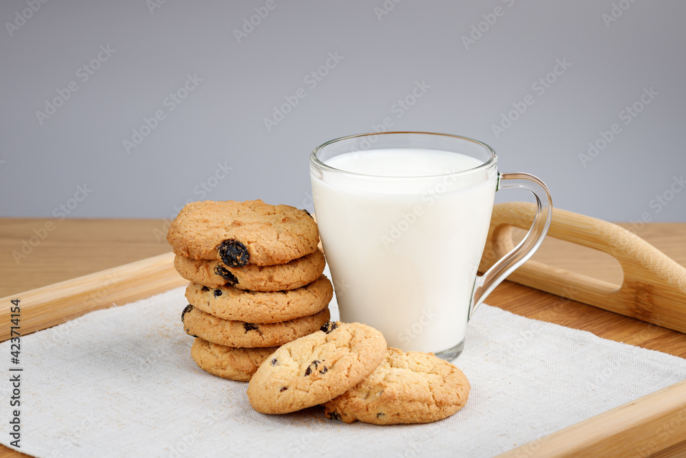 Cup of milk and cookies with raisins on a wooden tray Cup of milk and cookies with raisins on a wooden tray