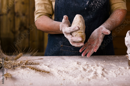 Women's hands, flour and dough. A woman in an apron is preparing dough for home baking. Rustic style photo. Wooden table, wheat ears and flour. Emotional photo. Cozy atmosphere