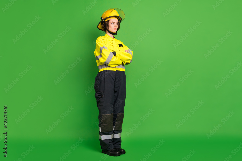 Fototapeta premium Full length photo of pretty adorable fire lady workwear yellow helmet arms folded looking empty space isolated green color background