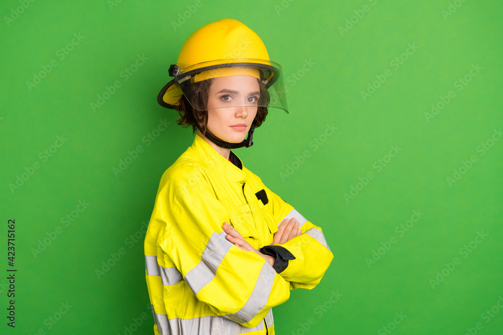 Photo of cute serious young firewoman dressed yellow uniform helmet arms crossed empty space isolated green color background Photo of cute serious young firewoman dressed yellow uniform helmet arms crossed empty space isolated green color background