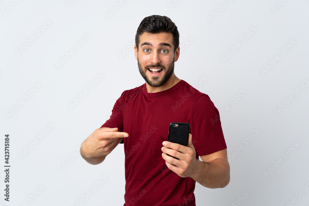 Young handsome man with beard using mobile phone isolated on white background and pointing it Young handsome man with beard using mobile phone isolated on white background and pointing it