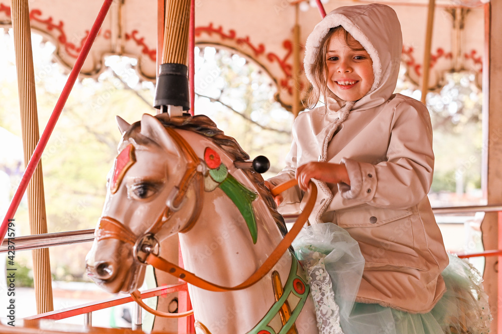 A little girl in bright clothes rides on the carousel with animals. Happy child