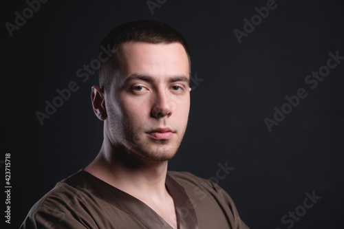 young man with stubble and short hair in a shirt on a dark background, portrait