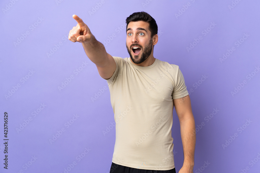 Fototapeta premium Young handsome man with beard over isolated background pointing away