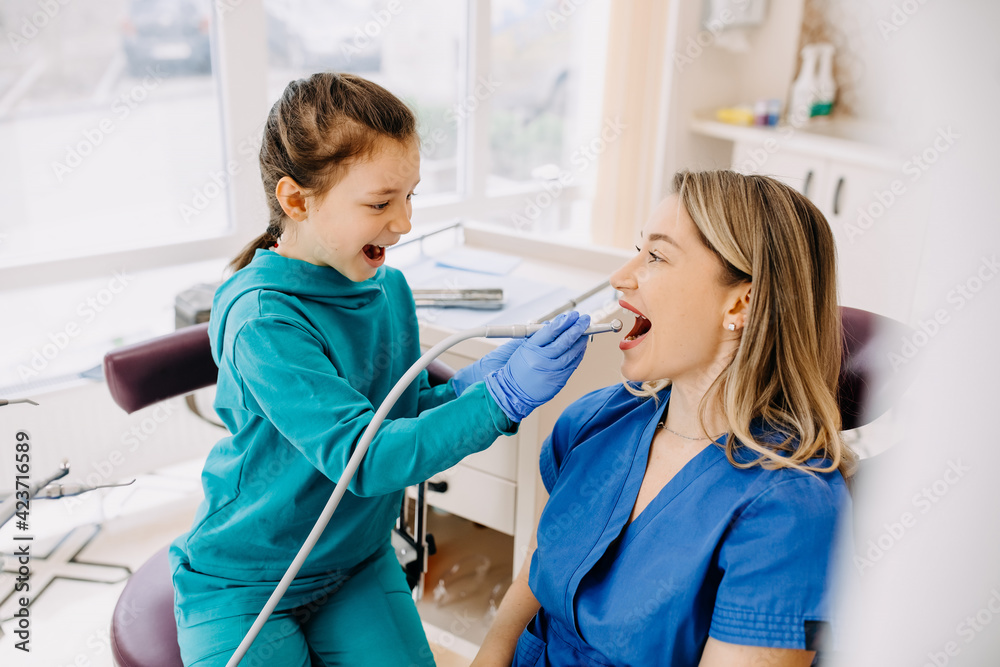 Little girl doctor with a patient at a dental clinic checking teeth. 