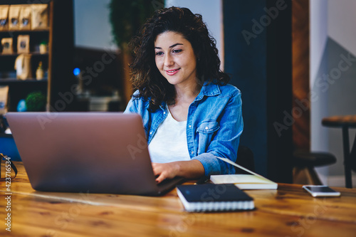 Skilled hipster girl reading text publication and browsing media content during social networking via netbook app, Caucaisan female freelancer doing distance job on modern netbook connecting to 4g photo