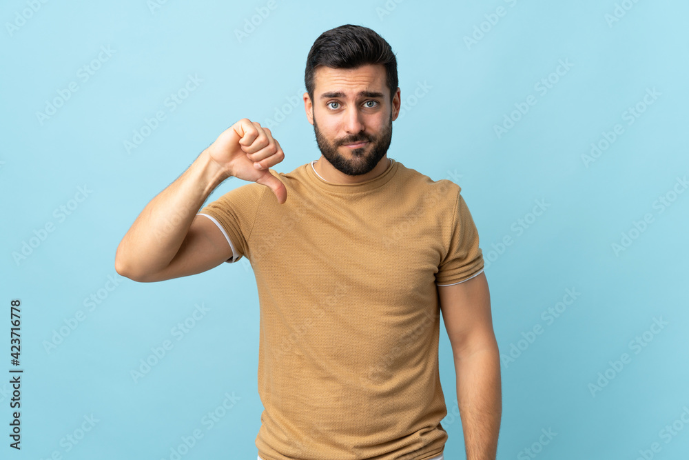 Young handsome man with beard over isolated background showing thumb down with negative expression Young handsome man with beard over isolated background showing thumb down with negative expression