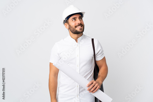 Young architect man with helmet and holding blueprints isolated on white background thinking an idea while looking up