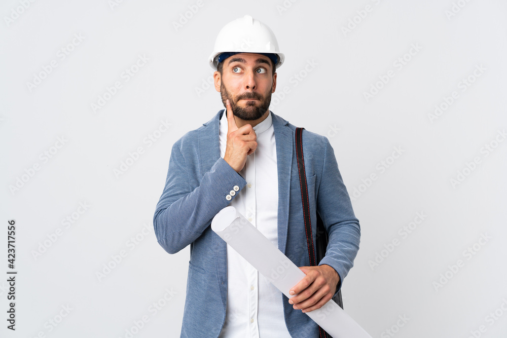 Young architect man with helmet and holding blueprints isolated on white background having doubts and thinking Young architect man with helmet and holding blueprints isolated on white background having doubts and thinking