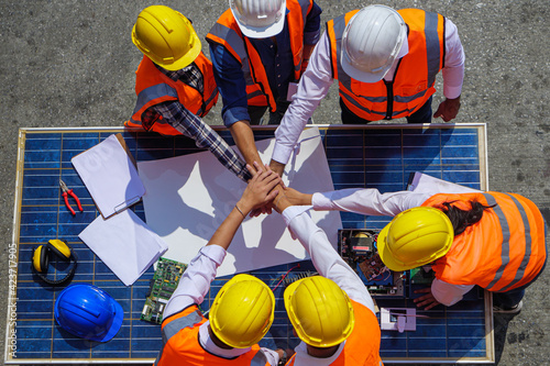 Top view of Architectural engineers putting their hands together on solar panel and his blueprints with Solar photovoltaic equipment on construction site. meeting, discussing, designing, planing photo