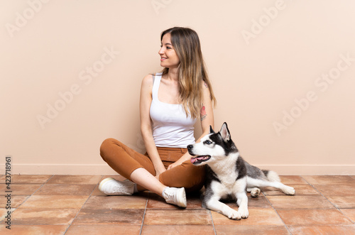 Young pretty woman with her husky dog sitting in the floor at indoors looking side